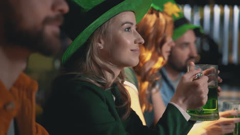 Friends-Celebrating-Saint-Patrick's-Day-In-A-Pub,-Smiling-Happy-Woman-Looks-At-Camera