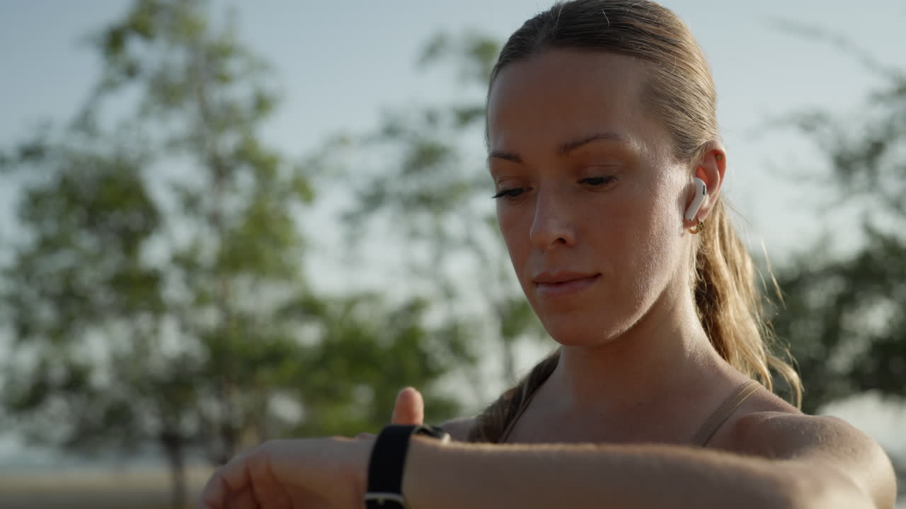 Giovane donna che controlla lo smartwatch con auricolari wireless all'aperto