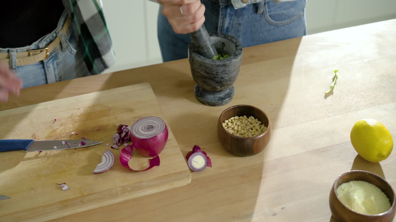 African American women starting at counter grinding herbs in mortar, chopping garlic for sauce