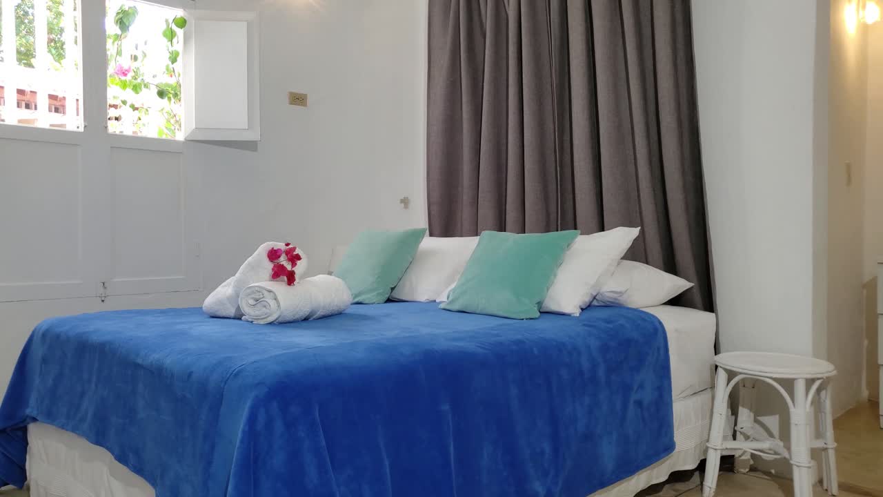 Cozy bedroom featuring a bed with a blue blanket, white and blue pillows, rolled towels, tilt down