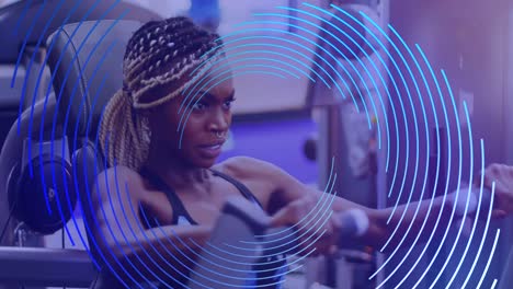 Animation-of-blue-line-spiral-rotating-over-african-american-woman-exercising-at-gym