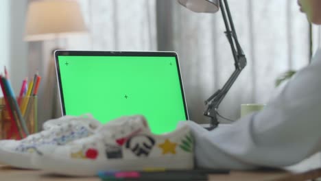 person working on a laptop with green screen and decorated shoes