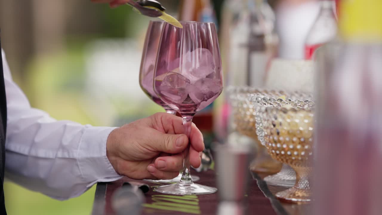 Close up of lemon being poured into pink glasses with ice at a cocktail bar