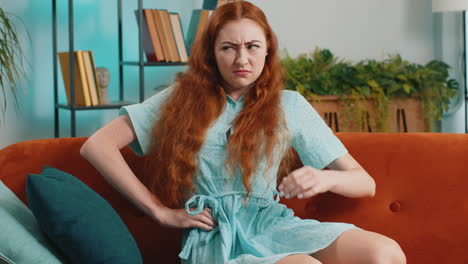 woman sitting on a couch, looking away, holding her stomach, looks sad