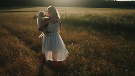 woman carrying a puppy in a golden field at sunset