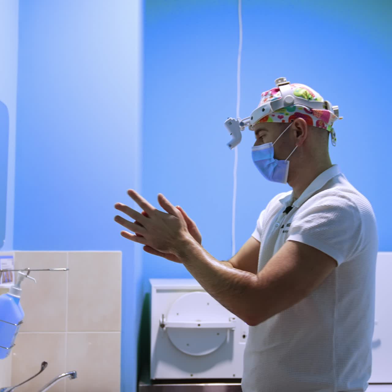 Surgeon in bright cap, mask and headlight covers the hands with antiseptic. Doctor's preparation for the operation