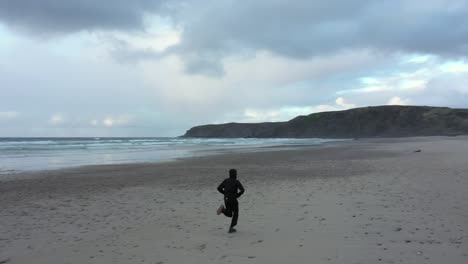 Hombre-Despreocupado-Disfrutando-Corriendo-Con-Los-Brazos-Abiertos-En-La-Playa-De-Playa-De-Xago-Temprano-En-La-Mañana-En-Asturias,-España