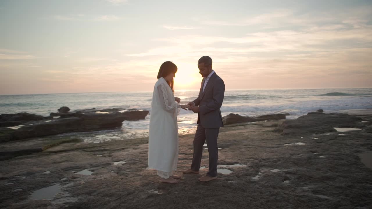 Groom putting ring on finger of bride on sea shore