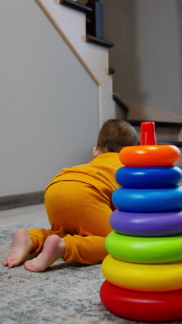 sweet little kid plays with a toy pyramid. child takes one ring and crawls away. house indoor backdrop. vertical video