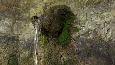 Schöner-Alter-Brunnen-Mit-Kaltem-Wasser,-Das-Aus-Geschnitztem-Stein-Fällt,-Umgeben-Von-Moos