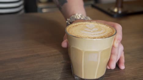 male hand serving a glass of latte at coffee bar counter