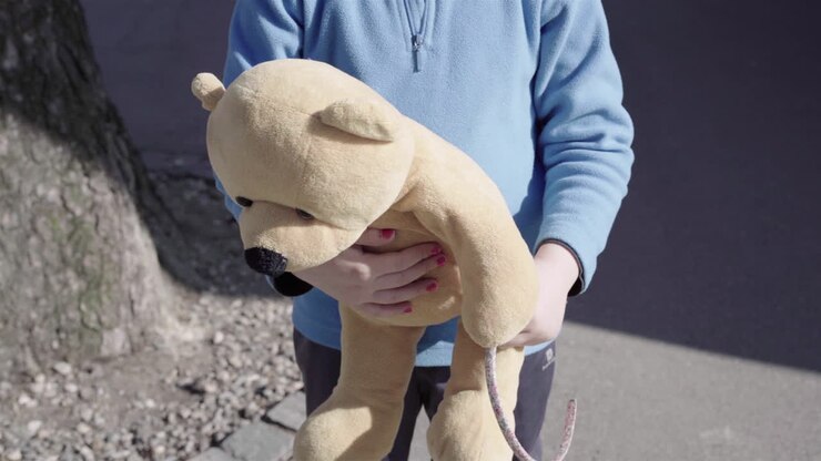 Close-up seorang gadis kecil dengan cat kuku biru memeluk boneka beruangnya di luar ruangan 4k.