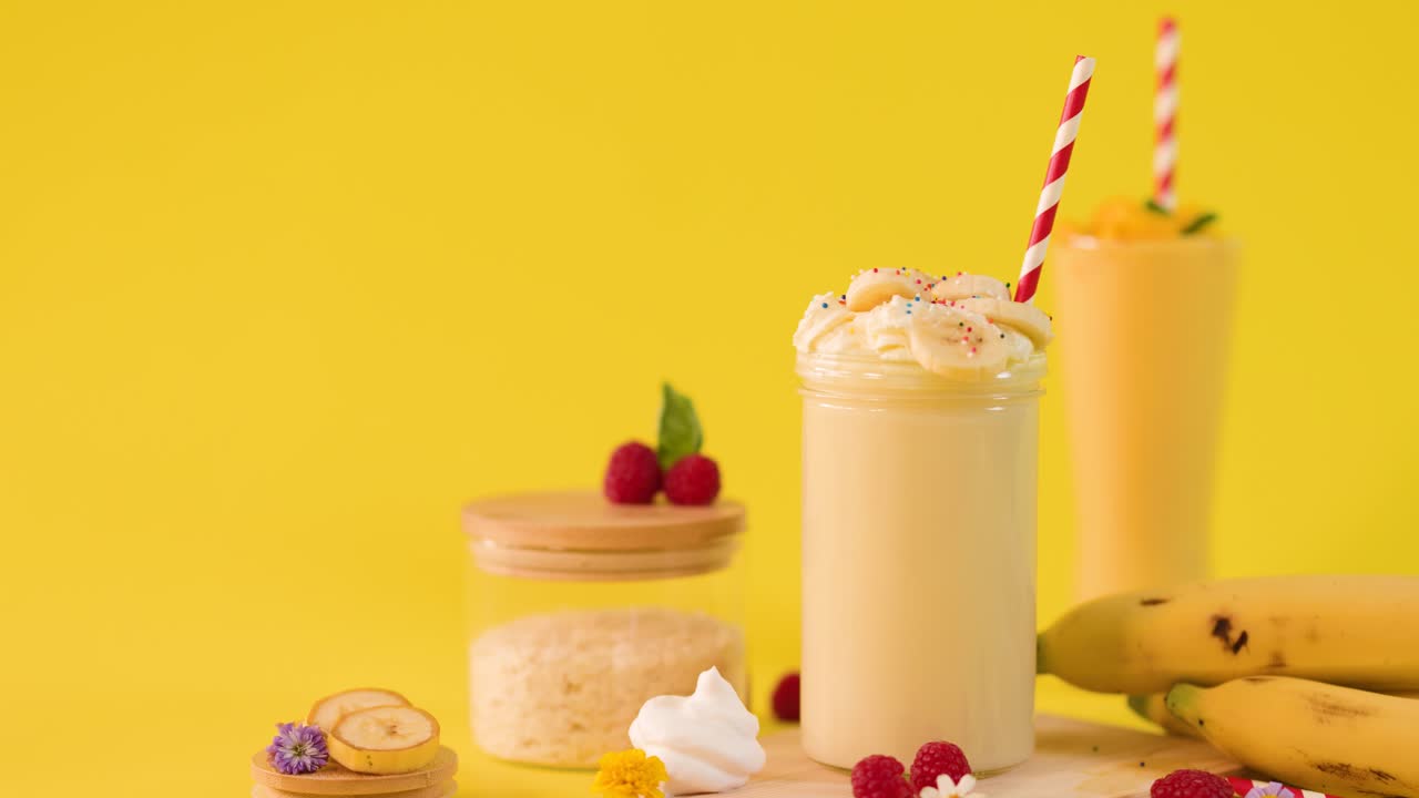 Una mano decora un cremoso smoothie alla banana con un ombrellino su sfondo giallo brillante, primo piano statico
