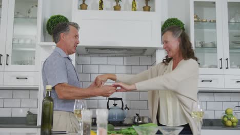 Feliz-Pareja-Caucásica-Mayor-Divirtiéndose-Bailando-En-La-Cocina-Y-Sonriendo