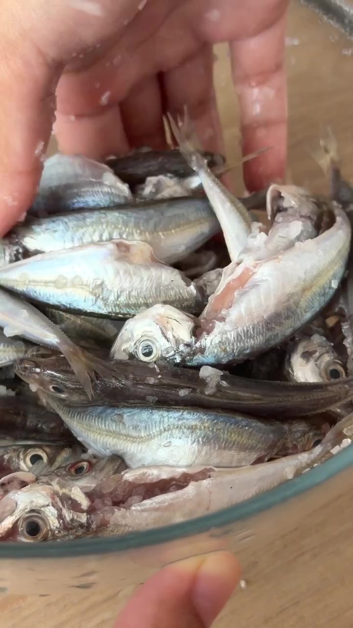 Person Seasoning Fresh Small Fish with Salt in a Glass Bowl