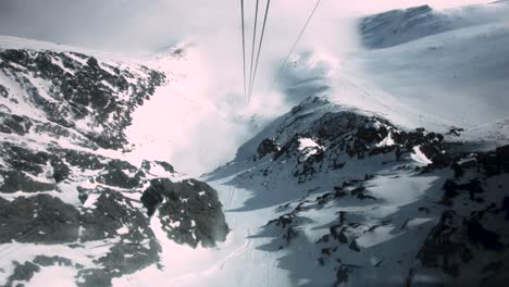 pov of ski lift moving down snowy trail on cables between jagged peaks