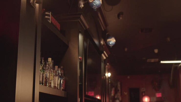 Luci disco multicolori illuminano gli scaffali in legno di un bar, bottiglie di alcol sullo scaffale.