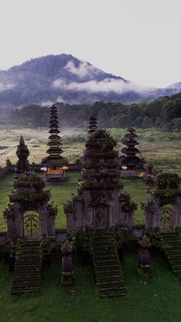 mist rises over tamblingan temple at dawn as a vertical drone reveals the serene lake setting and quiet nature of this sacred balinese site hidden in the highlands.