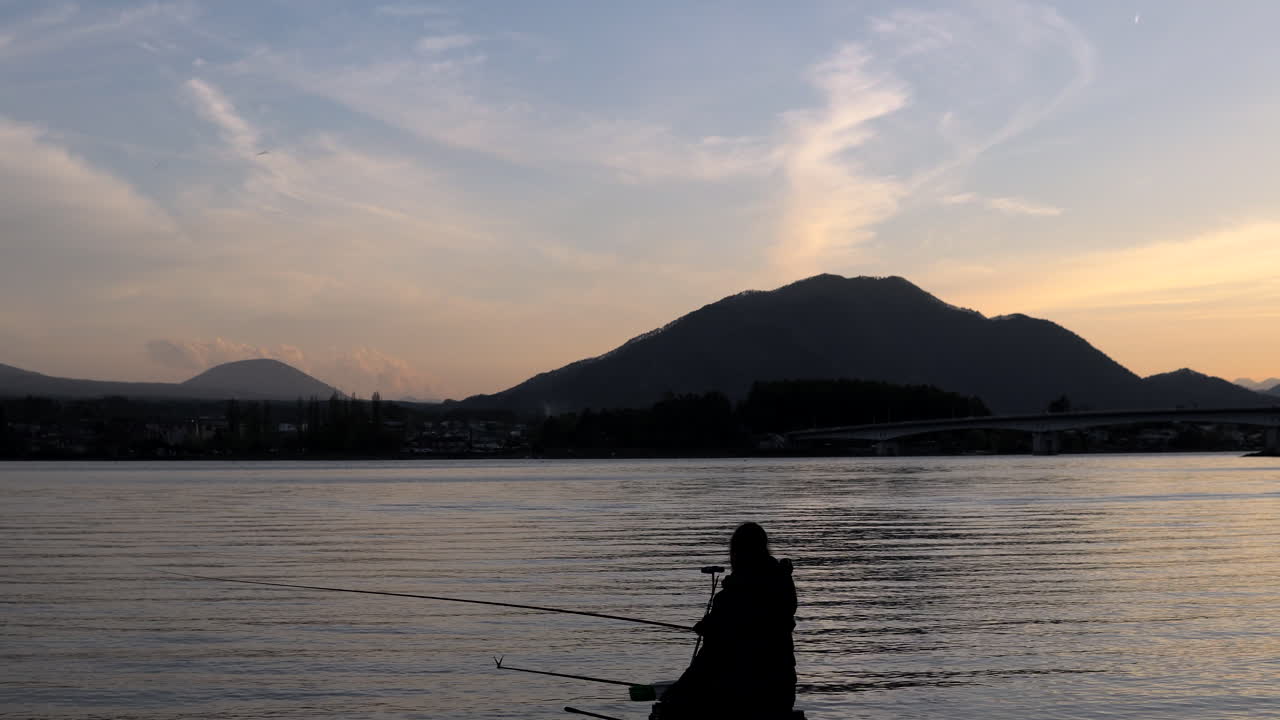 Wide handheld shot of a fishermann at Lake Kawaguchiko during sunset, Mt. Fuji, Japan