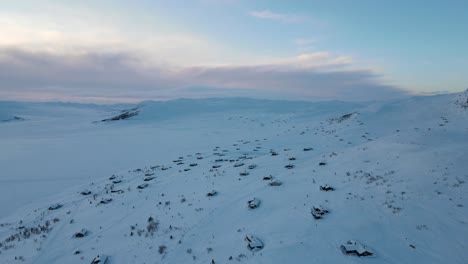 Holiday-cottages-covered-in-snow-on-a-shore-of-frozen-mountain-lake