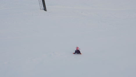 7 year girl with unicorn helmet have fun sliding down snowy hill, high angle handheld