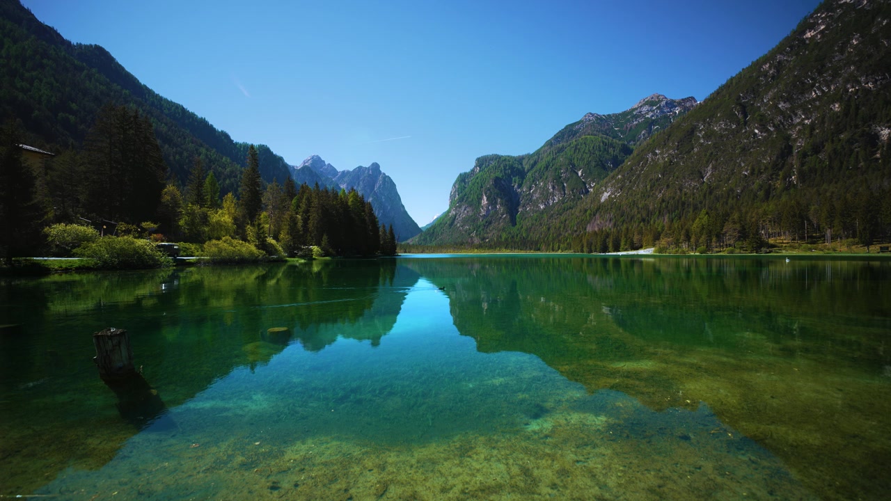 Vista di inizio estate sulle acque turchesi del Lago di Dobbiaco verso il lontano massiccio del Monte Cristallo, Italia