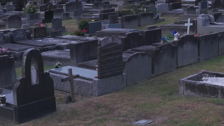 Esplora un cimitero tranquillo a Ferntree Gully, Melbourne, durante l'ora d'oro. Questa scena serena immortala fiori, lapidi e il tenue sole al tramonto, senza persone presenti.