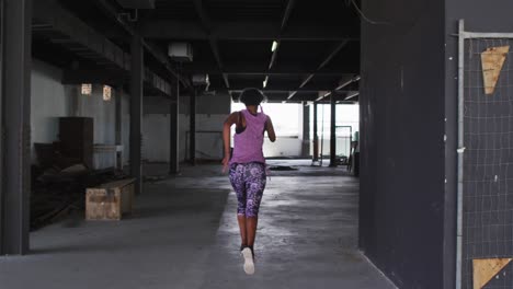 African-american-woman-wearing-sports-clothing-jogging-through-an-empty-urban-building