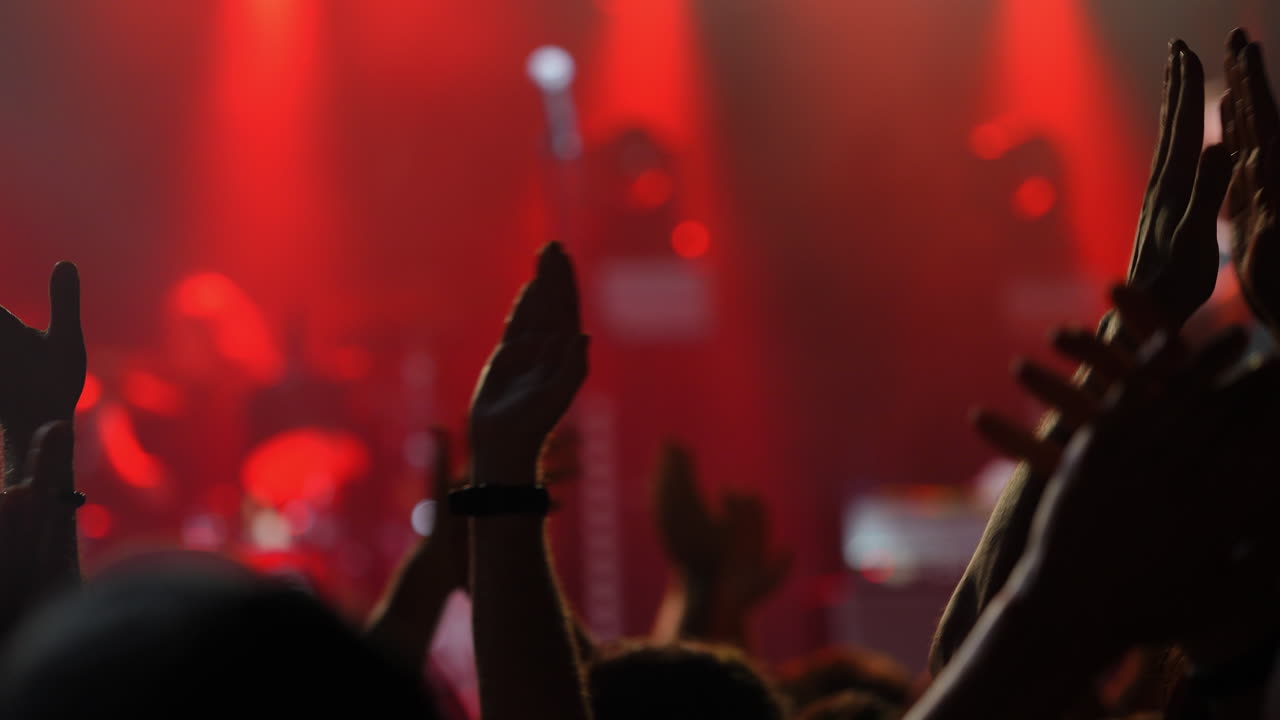 Público aplaudindo com entusiasmo em um concerto de música ao vivo com iluminação vermelha vibrante.