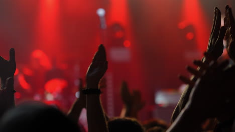 audience clapping hands in excitement at a live music concert with vibrant red lighting