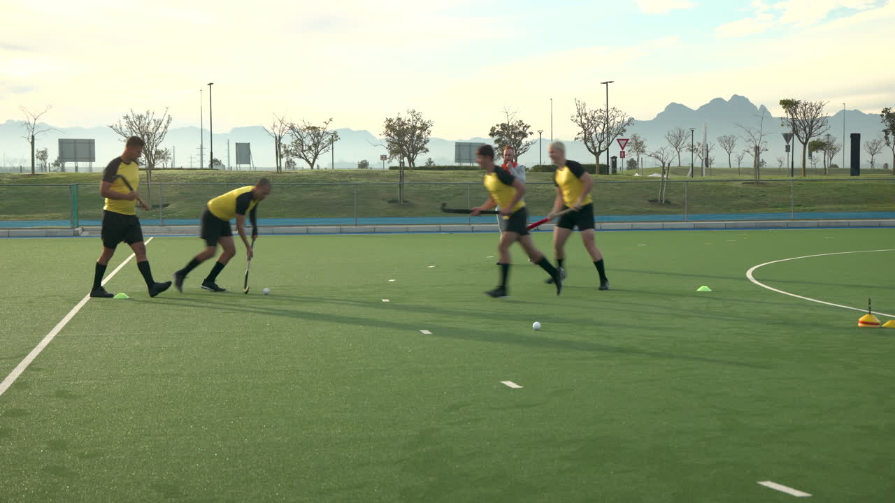 Playing field hockey, male athletes practicing on outdoor field with coach observing