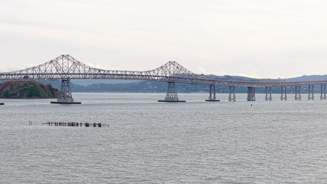 Calm waves reflect the afternoon light beneath the Richmond–San Rafael Bridge, as seen from a drifting aerial vantage.