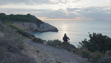 Cyclist-pushes-bike-along-small-rocky-trail-with-a-stunning-beach-view-in-early-morning-light