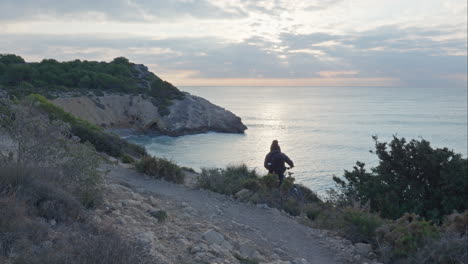 cyclist pushes bike along small rocky trail with a stunning beach view in early morning light