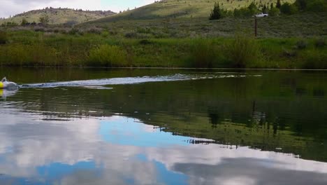 a fishing hook is seen skipping across the top of a pond with a green meadow in the background