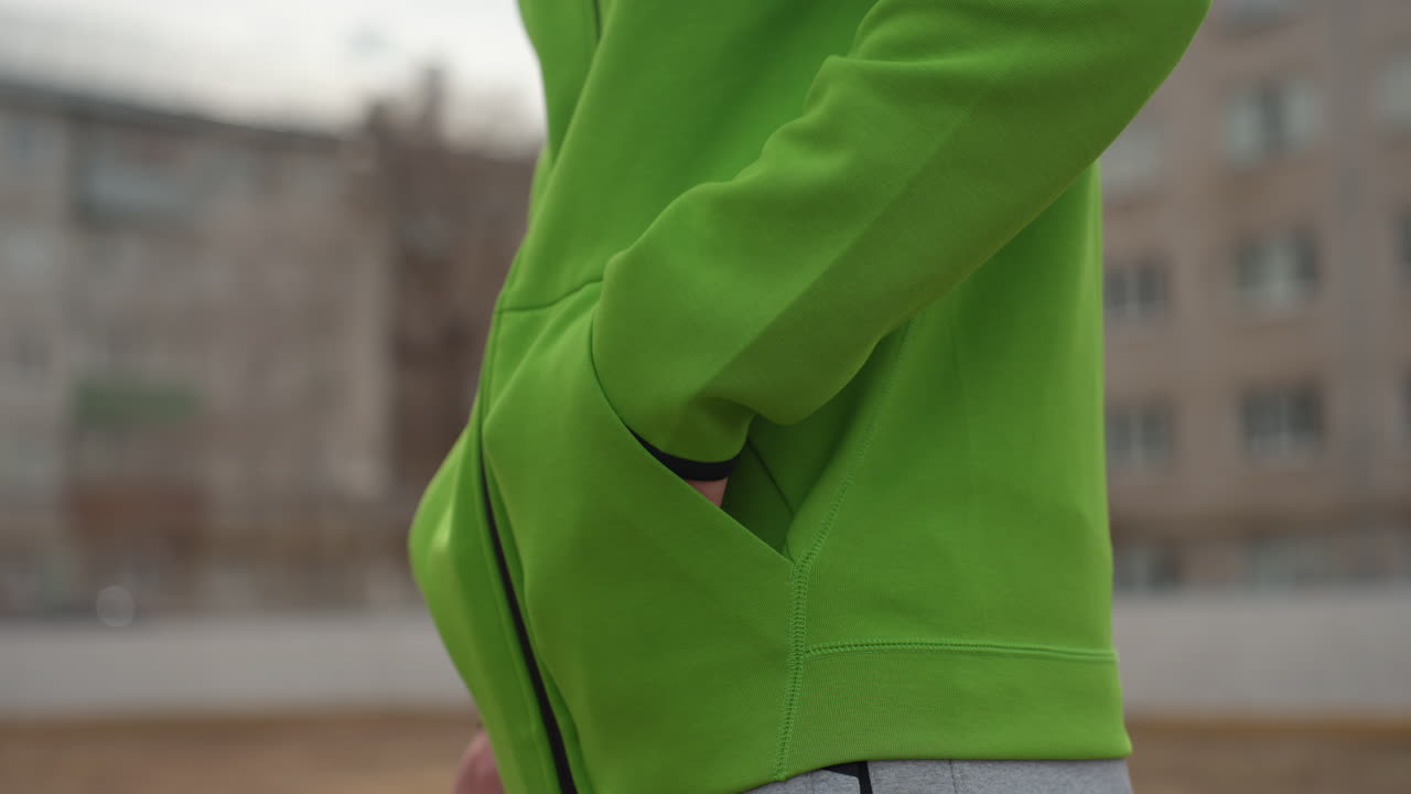 Persona con sudadera con capucha, hombre con sudadera verde con teléfono, viajero con sudadera verde usando el teléfono en la ciudad, escena urbana con hombre con sudadera con capucha usando un smartphone con las manos en primer plano