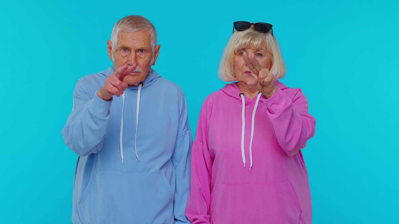 Senior couple man woman grandparents pointing at eyes and camera, show I am watching you gesture