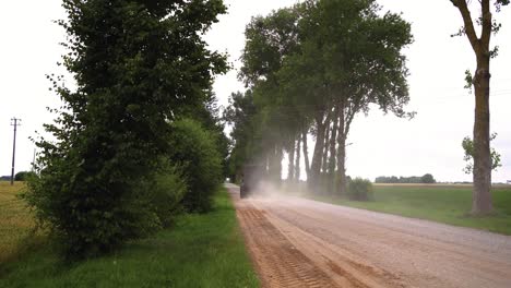 shot of tractor driving on a dirt road with trees and bright sky, sliding shot