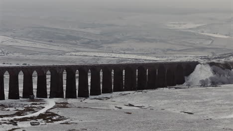 establishing aerial drone shot of snowy yorkshire dales and ribblehead viaduct in winter on misty day uk