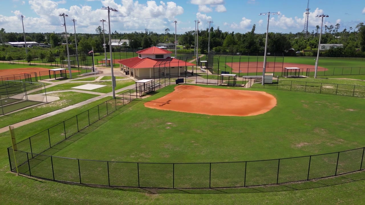 Ripresa aerea con drone in allontanamento di un piccolo parco sportivo con campi da baseball e un edificio per le concessioni.