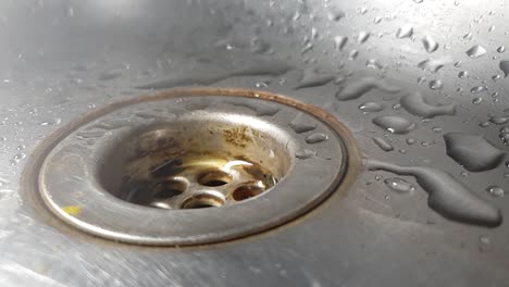 faucet drainage hole in stainless kitchen sink with water dripping and splashing droplets in slow motion