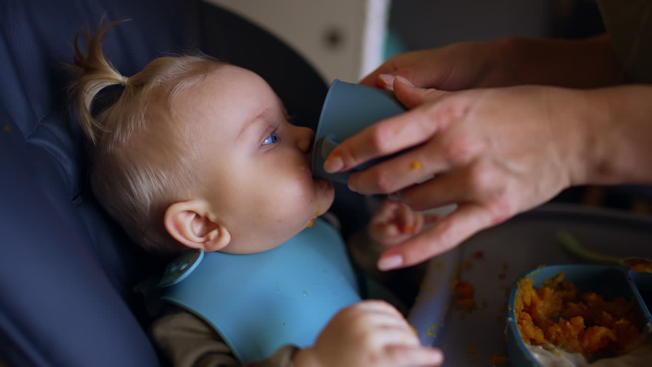 Unrecognized woman giving a cup with a drink to her baby. Little kid coughs after drinking. Close up.