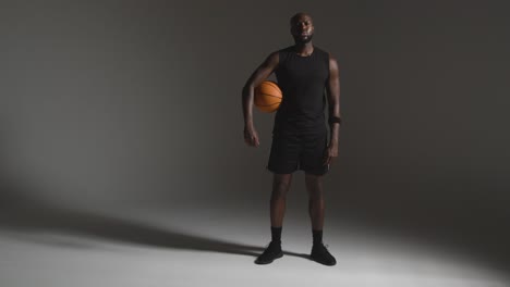 full length studio portrait shot of male basketball player holding ball under arm against dark background