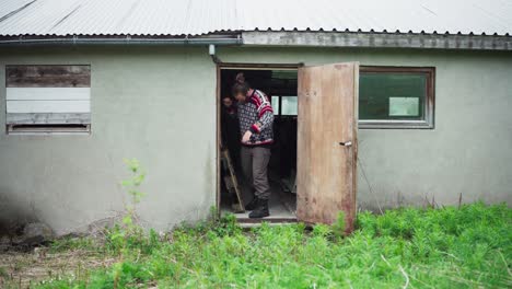 man inside the house opens old damaged door and came out with wooden pallet into the backyard