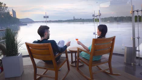 Pareja-Brindando-Con-Vino-Sentado-En-La-Terraza-Del-Restaurante-Junto-Al-Río-Danubio