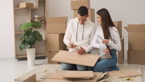 front view of a young couple in a new house sitting on the carpet assembling a furniture