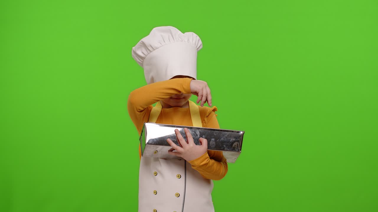 Bambina pasticcera con grembiule e cappello che aggiunge uvetta all'impasto in una ciotola, preparando pane o una torta.