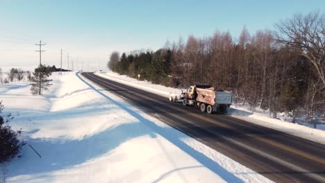 Aerial-view-of-a-municipal-snow-plow-clearing-snow-on-a-rural-highway-after-the-storm-on-a-bright-sunny-morning