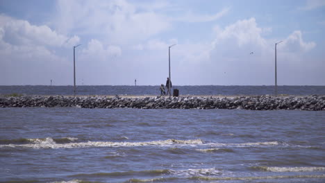 a father and son walk along a stone pier in with fishing gear in hand on a beautiful, sunny day in gulfport, mississippi