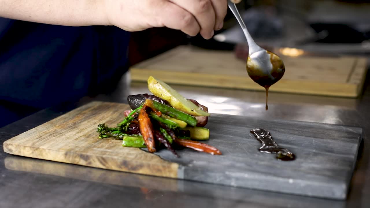 chef con cuchara vertiendo tamari demi-glace junto a las verduras chamuscadas
